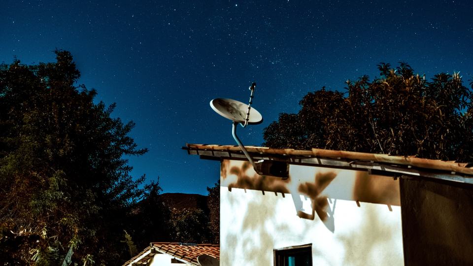 A satellite dish on a roof under a night sky
