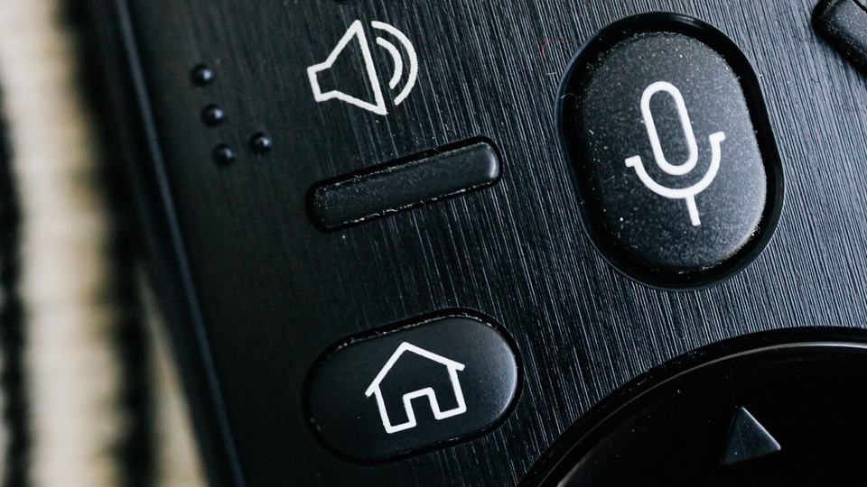 A remote control with home and voice buttons, close up