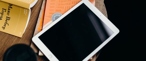 A tablet on a table, screen off, next to a book