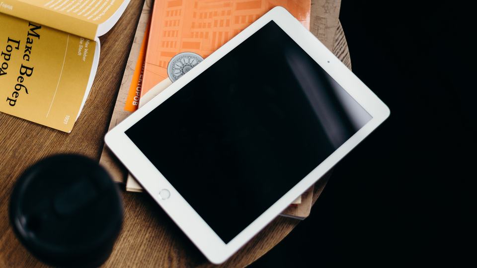 A tablet on a table, screen off, next to a book